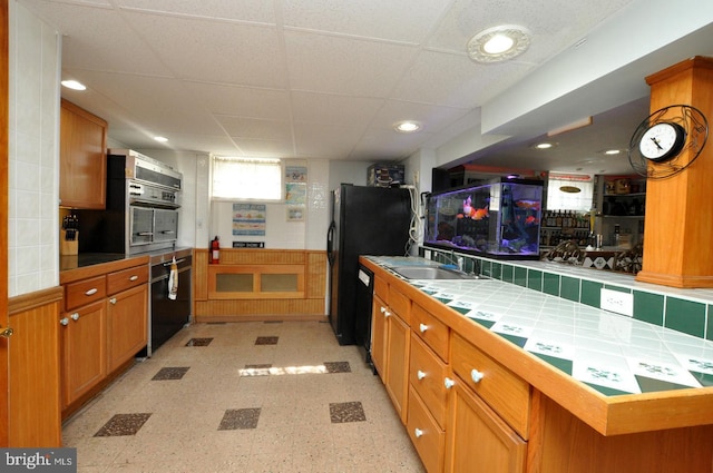 kitchen with oven, a drop ceiling, tile countertops, freestanding refrigerator, and a sink