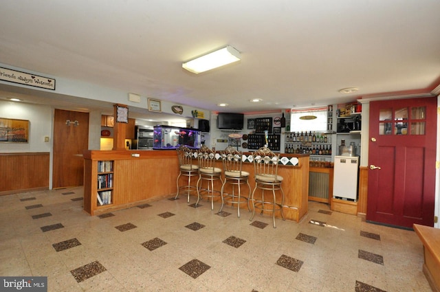 kitchen with tile patterned floors, a kitchen breakfast bar, wooden walls, a peninsula, and wainscoting