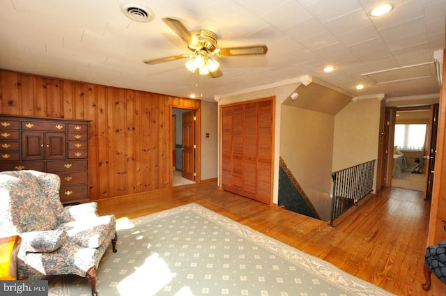 unfurnished room featuring visible vents, ornamental molding, a ceiling fan, wood finished floors, and wooden walls