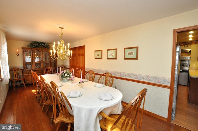 dining room with a chandelier, a wainscoted wall, dark wood finished floors, and wallpapered walls