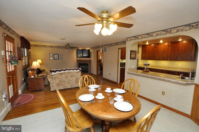 dining room featuring a ceiling fan, visible vents, baseboards, light wood finished floors, and a large fireplace