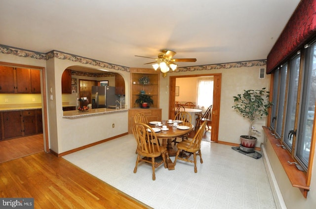 dining area featuring visible vents, light wood-style flooring, arched walkways, baseboards, and ceiling fan