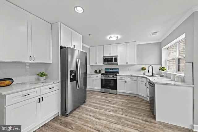 kitchen featuring visible vents, white cabinets, stainless steel appliances, crown molding, and a sink