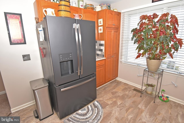 kitchen featuring stainless steel refrigerator with ice dispenser, brown cabinets, and baseboards