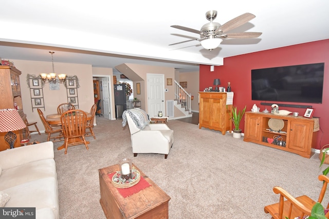 carpeted living room with ceiling fan with notable chandelier and stairway