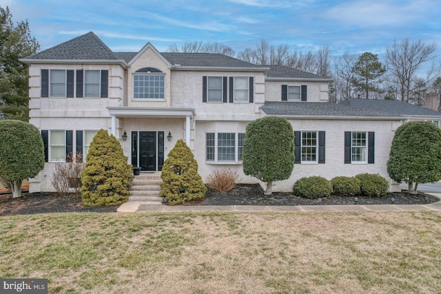 view of front of house with stucco siding, a shingled roof, and a front yard