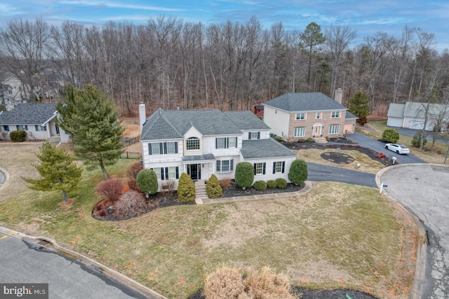 exterior space with a view of trees, a front lawn, a chimney, and aphalt driveway