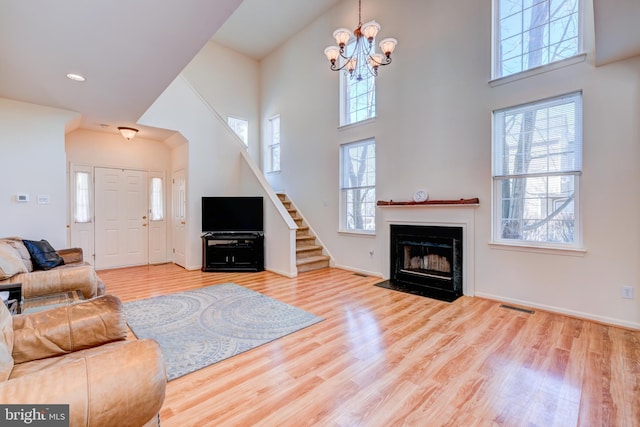 living area featuring a notable chandelier, light wood finished floors, visible vents, a high ceiling, and a fireplace with flush hearth