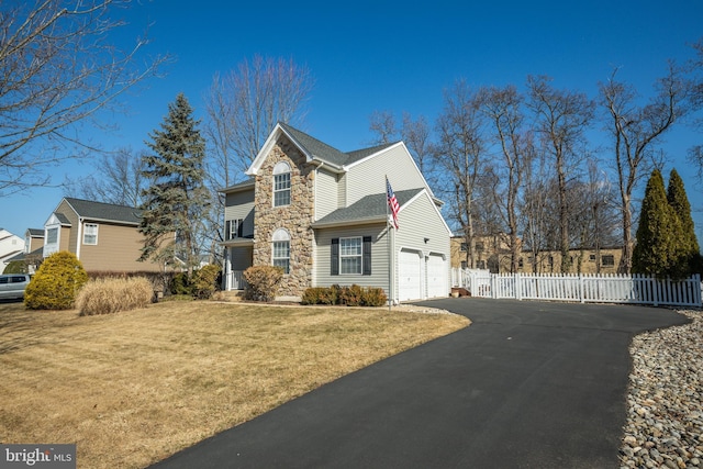 traditional home with aphalt driveway, fence, a garage, stone siding, and a front lawn