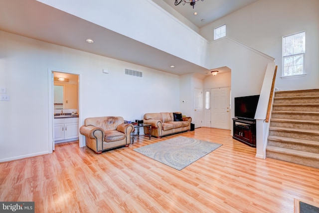 living room featuring recessed lighting, visible vents, a towering ceiling, light wood-type flooring, and stairs