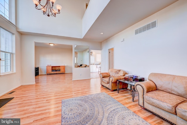 living area featuring light wood finished floors, a towering ceiling, visible vents, and a notable chandelier