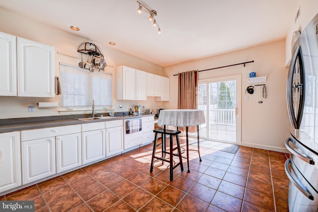 kitchen with a sink, white cabinetry, a kitchen breakfast bar, freestanding refrigerator, and dark countertops