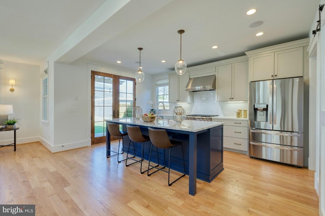 kitchen with light wood-style floors, a kitchen breakfast bar, stainless steel appliances, wall chimney range hood, and backsplash