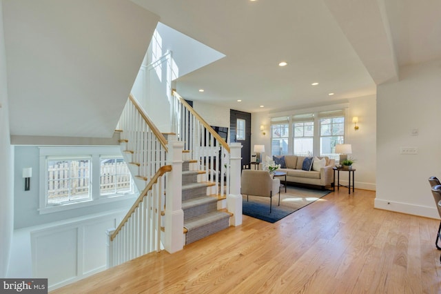 stairway featuring a healthy amount of sunlight, a decorative wall, wood finished floors, and recessed lighting