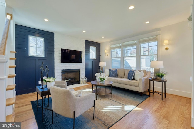 living area featuring a large fireplace, baseboards, wood finished floors, and recessed lighting