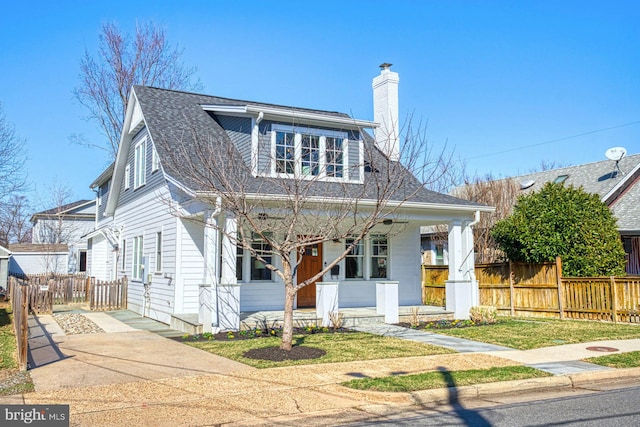 view of front facade with covered porch, a shingled roof, a chimney, and fence