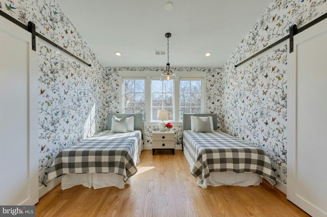 bedroom featuring recessed lighting, visible vents, a barn door, wood finished floors, and wallpapered walls