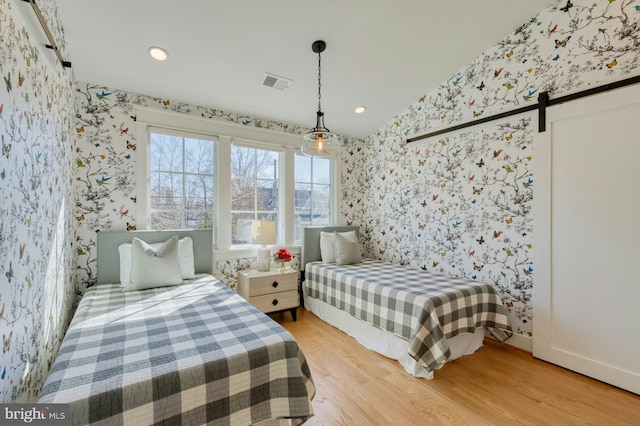 bedroom with wallpapered walls, a barn door, visible vents, light wood-type flooring, and recessed lighting