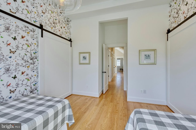 bedroom with light wood-style floors, a barn door, and baseboards