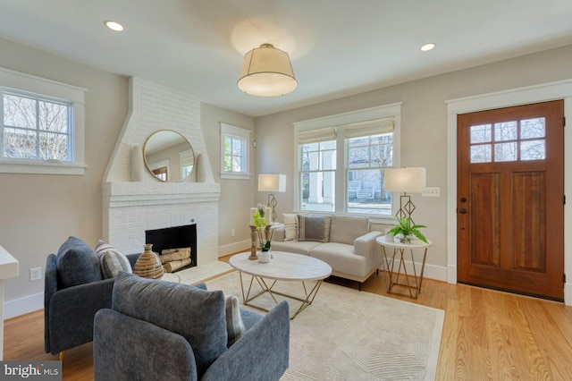 living area featuring recessed lighting, a brick fireplace, baseboards, and light wood finished floors