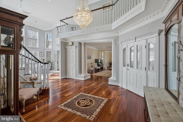 entryway with dark wood finished floors, crown molding, a high ceiling, ornate columns, and stairs