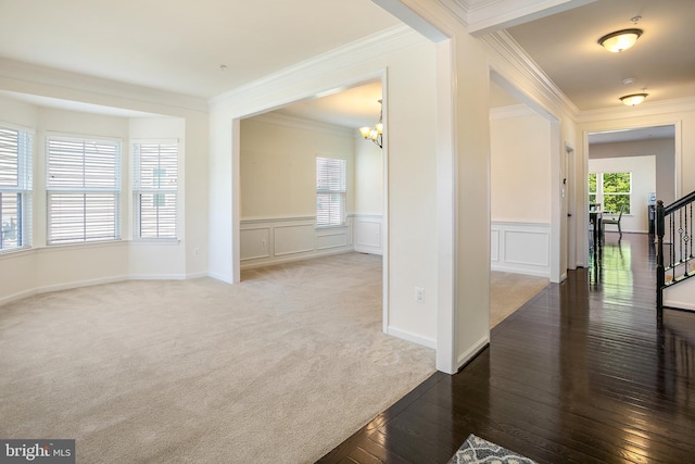carpeted foyer featuring a chandelier, wood-type flooring, crown molding, stairs, and a decorative wall
