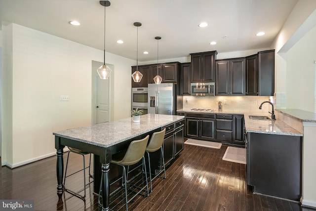 kitchen featuring light stone countertops, stainless steel appliances, a sink, dark wood-style floors, and a center island
