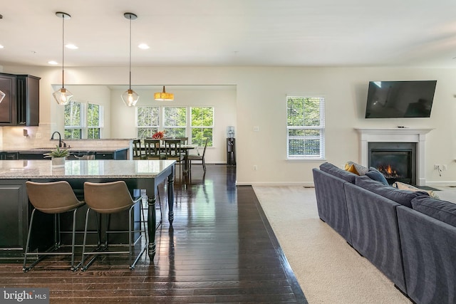 kitchen featuring a glass covered fireplace, dark wood-type flooring, light stone counters, baseboards, and open floor plan