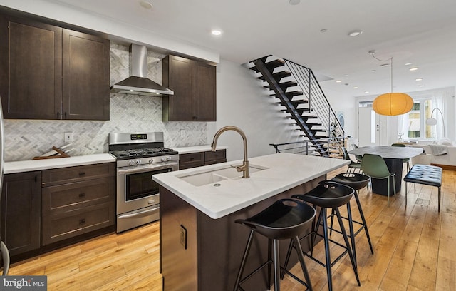 kitchen with hanging light fixtures, an island with sink, wall chimney range hood, stainless steel range with gas cooktop, and sink