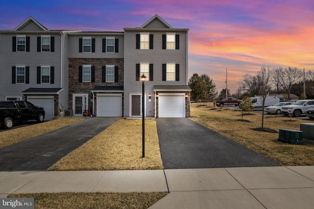 townhome / multi-family property featuring stone siding, driveway, and an attached garage