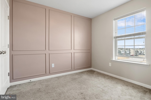 carpeted empty room featuring a decorative wall and baseboards