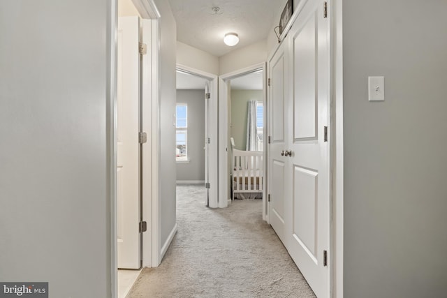 hallway featuring light carpet and baseboards