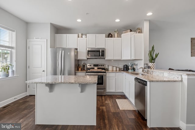 kitchen featuring a breakfast bar area, decorative backsplash, appliances with stainless steel finishes, white cabinets, and a sink