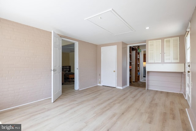 unfurnished living room featuring attic access, wood finished floors, and brick wall