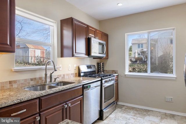 kitchen with appliances with stainless steel finishes, light stone countertops, baseboards, and a sink