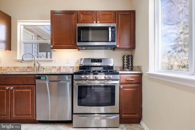 kitchen with light stone countertops, stainless steel appliances, baseboards, and a sink