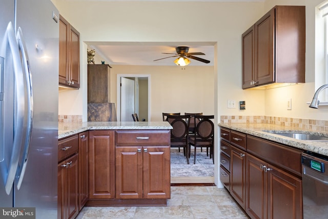 kitchen featuring light stone counters, a peninsula, ceiling fan, a sink, and appliances with stainless steel finishes