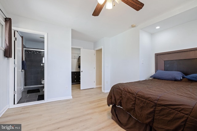 bedroom featuring a walk in closet, light wood-style flooring, a ceiling fan, ensuite bath, and baseboards