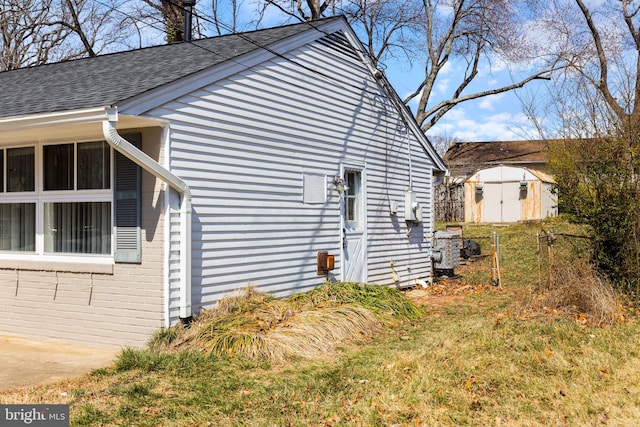 view of side of home with a shingled roof, brick siding, a storage shed, and an outdoor structure