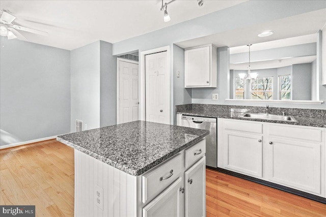 kitchen featuring stainless steel dishwasher, white cabinets, a kitchen island, a sink, and dark stone countertops