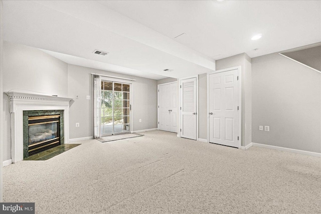 unfurnished living room with carpet floors, a high end fireplace, visible vents, and baseboards