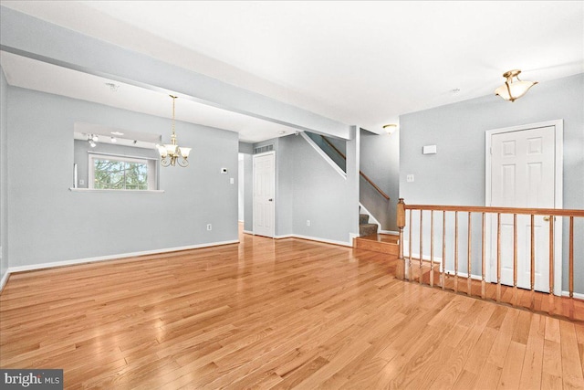 unfurnished room featuring light wood-type flooring, a notable chandelier, baseboards, and stairs