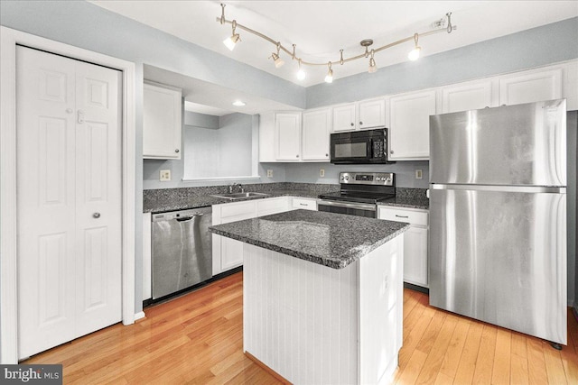 kitchen featuring light wood finished floors, stainless steel appliances, white cabinetry, a sink, and a kitchen island