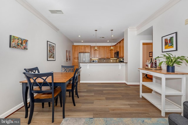 dining room featuring visible vents, crown molding, baseboards, and wood finished floors