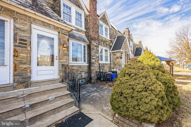 doorway to property featuring a patio, a chimney, and stone siding