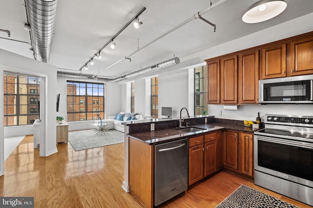 kitchen featuring stainless steel appliances, a peninsula, a sink, open floor plan, and dark stone countertops