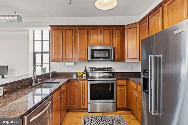 kitchen with dark stone counters, stainless steel appliances, a sink, and light wood-style floors