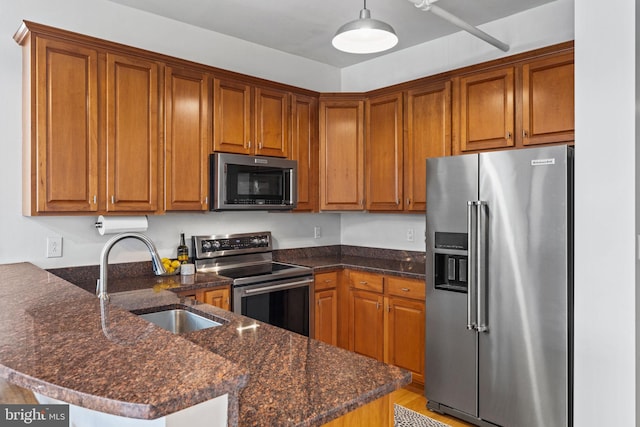 kitchen with brown cabinets, decorative light fixtures, appliances with stainless steel finishes, a sink, and a peninsula