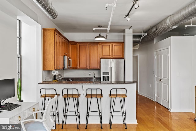 kitchen with a breakfast bar area, high end fridge, brown cabinetry, dark stone counters, and a peninsula