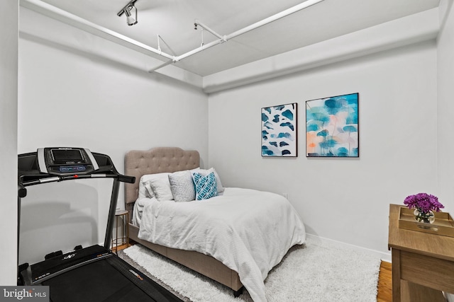 bedroom featuring rail lighting, baseboards, and wood finished floors